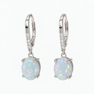 May include: A pair of silver-toned leverback earrings featuring oval-shaped white opals with iridescent flecks. The curved metal hooks are accented with small, clear, sparkling stones set in a vertical row above each dangling opal gemstone.