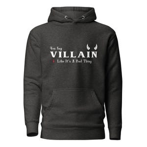 A heather black You Say Villain Like Its A Bad Thing hoodie with cute devil horns created by graphic apparel company Midnight Gypsy Designs as part of their Dark Academia clothing and Bookish Merch clothing line.