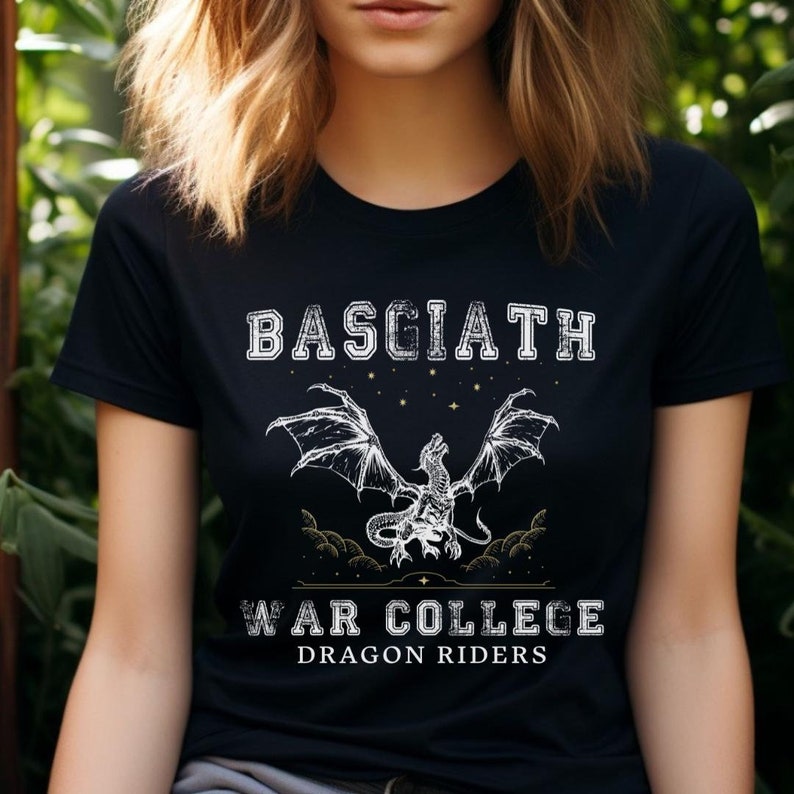 Young woman with blonde hair wearing a black Basgiath War College Dragon Riders shirt from Fourth Wing, Iron Flame, and Onyx Storm book designed by graphic apparel company Midnight Gypsy Designs for their Fantasy Bookish Merch collection.