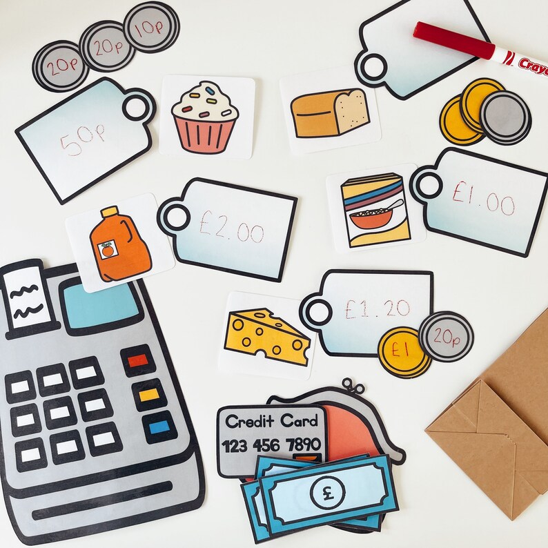K&ouml;nnte beinhalten: Eine Kasse mit einer Kreditkarte, Spielgeld und Preisschildern f&uuml;r einen Spielwarenladen. Die Preisschilder beinhalten Artikel wie einen Cupcake, Brot, M&uuml;sli, K&auml;se und Orangensaft. Die Preise sind in Britischen Pfund.