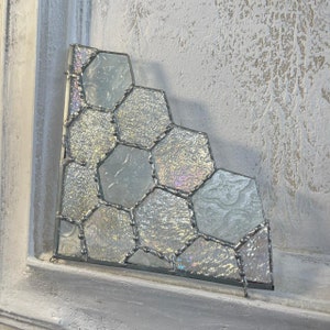 May include: A white stained glass piece with a honeycomb pattern. The glass is iridescent and has a silver frame.