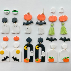 Op de afbeelding: Een verzameling Halloween-thema oorbellen. Ontwerpen omvatten geesten, pompoenen, vleermuizen en mummies in verschillende stijlen. De oorbellen zijn gemaakt van polymeerklei en hebben zwarte, witte, oranje en groene kleuren. Sommige oorbellen hebben goudkleurige accenten.