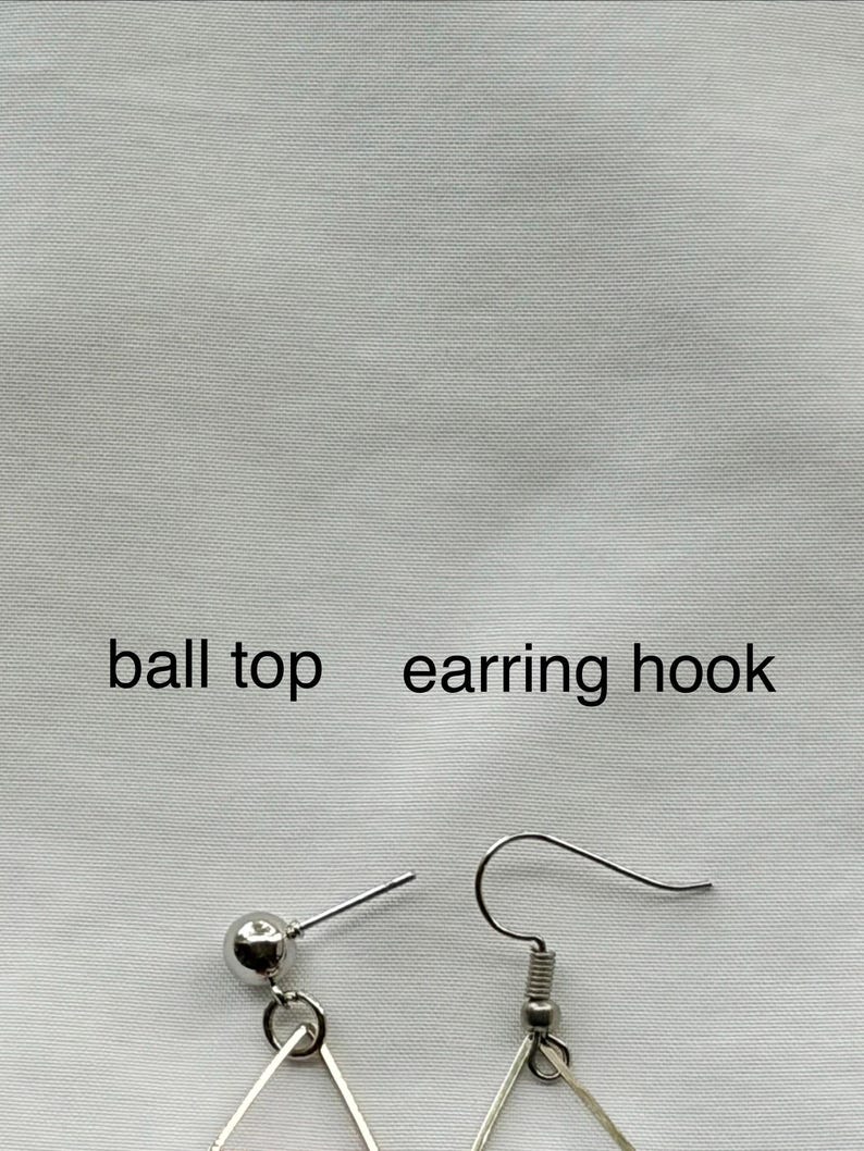 May include: Close-up of silver-colored earrings with a ball top and earring hook. The earrings have a geometric design. The text "ball top earring hook" is printed above the earrings.