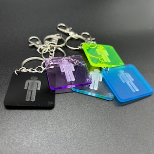 May include: A collection of keychains with a square shape and a man icon. The keychains come in various colors, including black, purple, green, and blue. Each keychain has a silver-colored clasp.