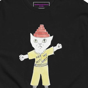 May include: Black t-shirt featuring a whimsical illustration of a cat wearing a red hat and yellow outfit. The cat has the text "ARE WE NOT CATS?" on its shirt. The Etsy shop name "SarahHausersFunhouse on etsy" is printed on the top.