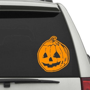 May include: Orange pumpkin with a carved jack-o'-lantern face on a car window.