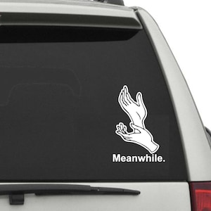May include: A white car window sticker with a black outline of two hands reaching up. The text "Meanwhile." is below the hands.