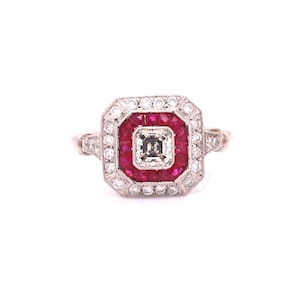 May include: A square-shaped ring with a central square-cut diamond surrounded by a halo of red rubies and a larger halo of smaller diamonds.