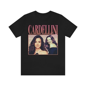 May include: Black t-shirt with a pink and white graphic of two women and the text "CARDELLINI Linda".