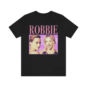 May include: Black t-shirt with a pink graphic of two women. The graphic includes the text "ROBBIE" in pink.