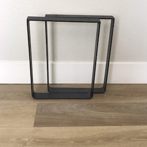 May include: Two black metal table legs with a rectangular shape. The legs are made of sturdy metal and have a simple, modern design.