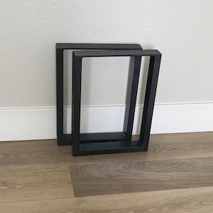 May include: Two black metal table legs, one stacked on top of the other. The legs are rectangular in shape and have a simple, modern design.