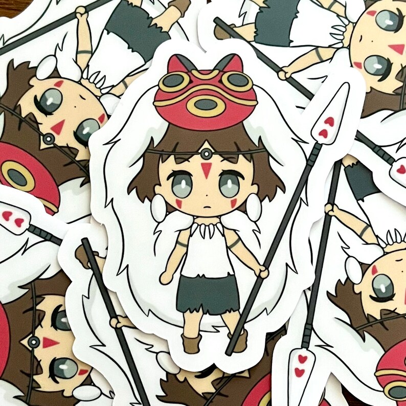 May include: A sticker featuring a cartoon character with brown hair, a red mask, and a white fur-like collar. The character is holding two spears with heart-shaped details. The sticker has a white border.