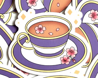 May include: A sticker featuring a teacup and saucer with a floral design. The teacup is purple with a white and gold trim, filled with tea and pink cherry blossoms. The saucer is white with a purple and gold trim.
