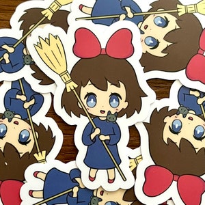 May include: A collection of stickers featuring a cartoon girl with brown hair, a red bow, and a blue dress, holding a broom. A small black cat is perched on her shoulder. The stickers are white with a glossy finish.