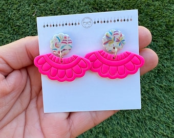 May include: Pink polymer clay earrings with a scalloped edge and a floral patterned charm hanging from the bottom.