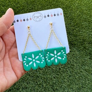 May include: Green and white dangle earrings with a floral design. The earrings have a gold chain and post. The earrings are on a white card with the text "SHOP SERENITY BY JAN".