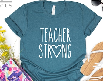 May include: Teal blue t-shirt with white text that reads "Teacher Strong" with a heart replacing the "O" in strong.