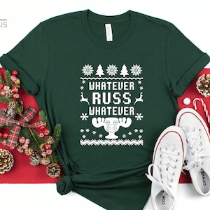 May include: A forest green t-shirt with a white Christmas-themed design featuring a moose and the text "Whatever Russ Whatever".