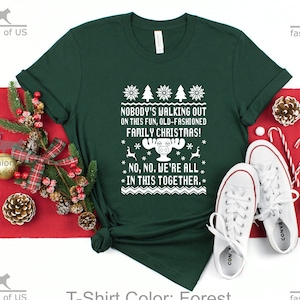 May include: Forest green t-shirt with a white Christmas-themed design. The design features a reindeer with the text "Nobody's walking out on this fun, old-fashioned family Christmas!" and "No, no. We're all in this together."