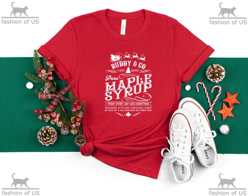 May include: Red t-shirt with a white graphic design that says "Bubby & Co. Est. 2003 Pure Maple Syrup Treat Every Day Like Christmas Packaged with 100% Christmas Cheer by Son of a Nutcracker Distributing".