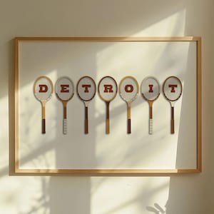 May include: A framed print with the word 'DETROIT' spelled out using vintage tennis rackets. The rackets are brown and white with red lettering.