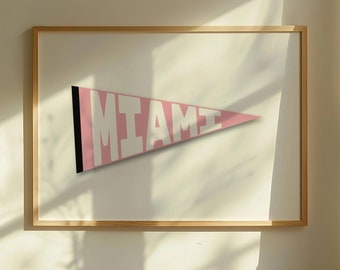 May include: A framed print of a pink pennant with the word "MIAMI" in white letters. The print is hanging on a white wall.