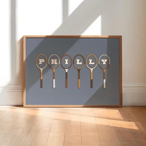 May include: A framed print with a blue background featuring six vintage tennis rackets with the word "PHILLY" spelled out using the rackets.