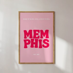 May include: A pink framed poster with the text "HOME OF BLUES, SOUL & ROCK 'N ROLL" at the top and "MEMPHIS" in large, pink, stylized letters in the center. The text "EST. 1819" is at the bottom of the poster.