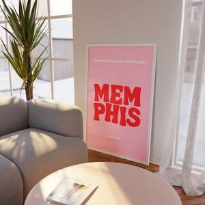 May include: Pink and white framed poster with the text "HOME OF BLUES, SOUL & ROCK 'N' ROLL" and "MEMPHIS" in red letters with "EST. 1819" below.