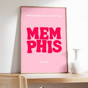 May include: Pink framed poster with the text "HOME OF BLUES, SOUL & ROCK 'N' ROLL" and "MEMPHIS" in large, bold, pink letters. The text "EST. 1819" is below the city name.