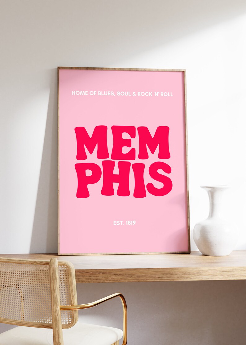 May include: Pink framed poster with the text "HOME OF BLUES, SOUL & ROCK 'N' ROLL" and "MEMPHIS" in large, bold, pink letters. The text "EST. 1819" is below the city name.