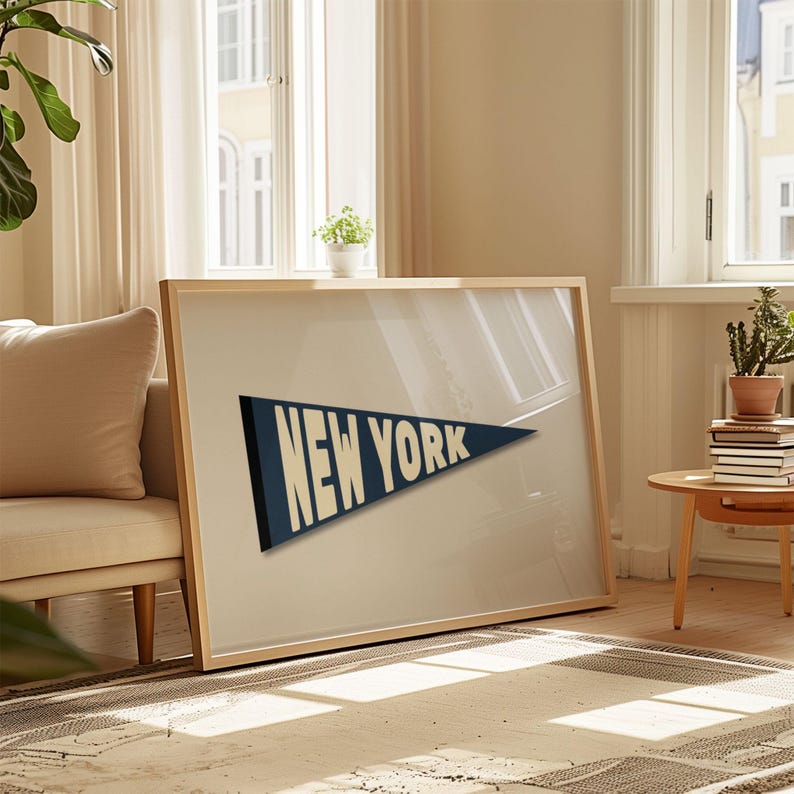 Puede incluir: Una impresi&oacute;n enmarcada de un bander&iacute;n azul con el texto "NEW YORK" en blanco. La impresi&oacute;n est&aacute; colgada en una pared en una habitaci&oacute;n con un sof&aacute; y una mesa auxiliar.