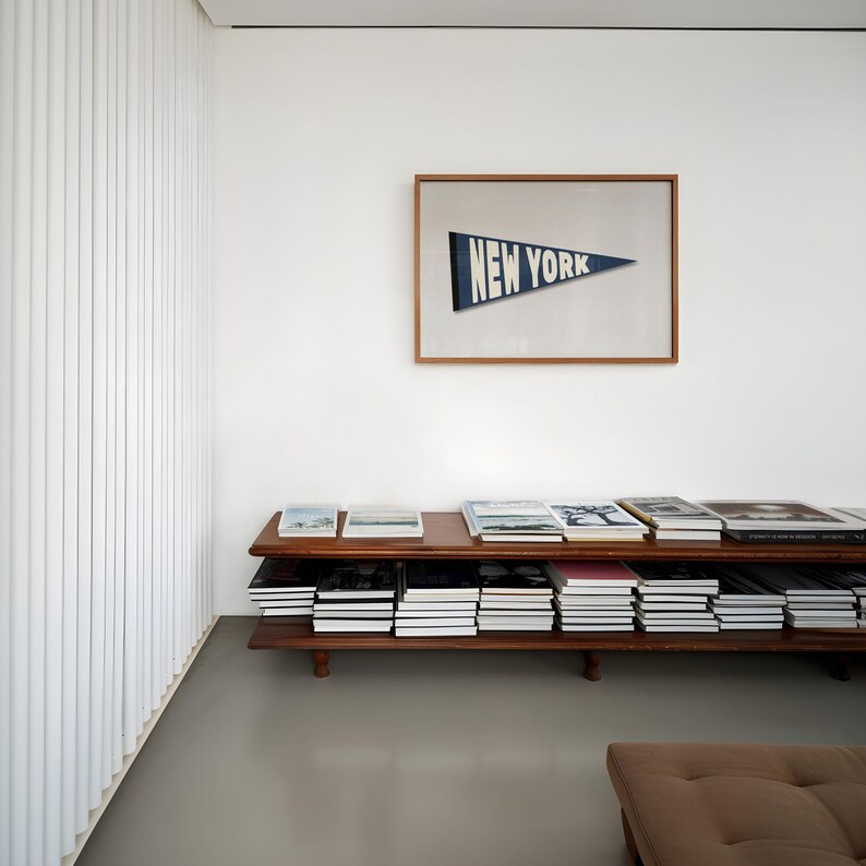 Puede incluir: Una estanter&iacute;a de madera con varios estantes llenos de libros. Un estampado enmarcado con el texto "NEW YORK" cuelga en la pared detr&aacute;s de la estanter&iacute;a.