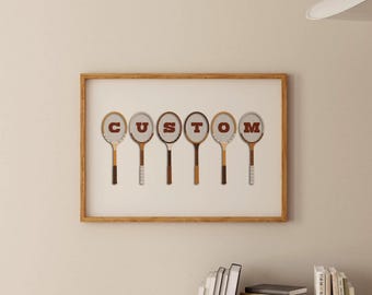 May include: A framed artwork featuring six vintage tennis rackets arranged to spell the word "CUSTOM" in red letters. The rackets have wooden handles and circular heads. The artwork is in a wooden frame.