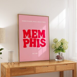 May include: A pink and white framed poster with the text "HOME OF BLUES, SOUL & ROCK 'N' ROLL" and "MEMPHIS" in large red letters. The poster also includes the text "EST. 1819".