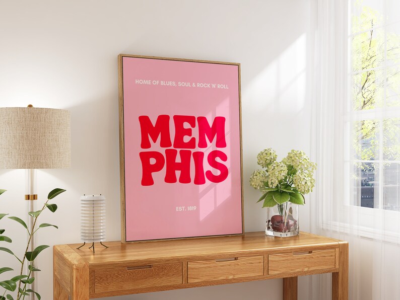 May include: A pink and white framed poster with the text "HOME OF BLUES, SOUL & ROCK 'N' ROLL" and "MEMPHIS" in large red letters. The poster also includes the text "EST. 1819".