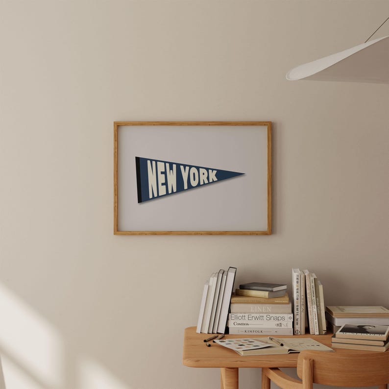 Puede incluir: Una impresi&oacute;n enmarcada de un bander&iacute;n azul con el texto "NEW YORK" en blanco. La impresi&oacute;n est&aacute; colgada en una pared de color beige claro.