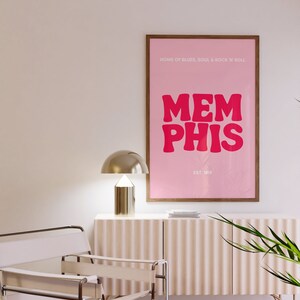 May include: A pink and brown framed poster with the text "HOME OF BLUES, SOUL & ROCK 'N' ROLL" and "MEMPHIS" in large pink letters. The text "EST. 1819" is below the word "MEMPHIS".