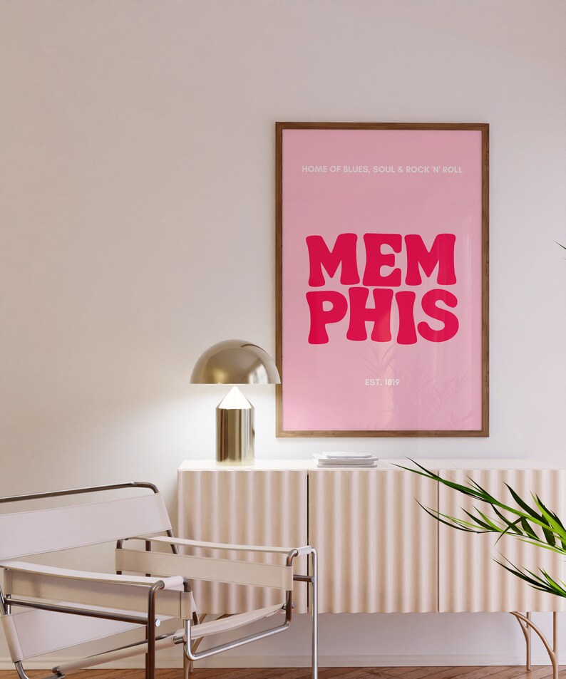May include: A pink and brown framed poster with the text "HOME OF BLUES, SOUL & ROCK 'N' ROLL" and "MEMPHIS" in large pink letters. The text "EST. 1819" is below the word "MEMPHIS".