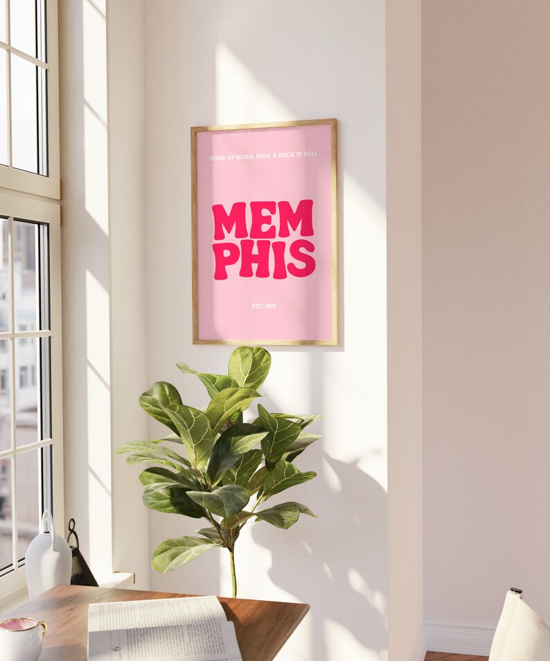 May include: A pink framed poster with the text "HOME OF BLUES, SOUL & ROCK N ROLL" and "MEMPHIS" in large pink letters. The text "EST. 1819" is below the word "MEMPHIS".