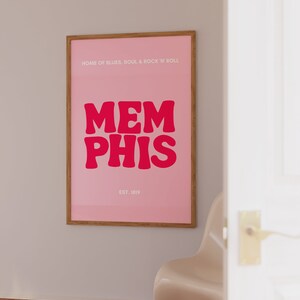 May include: A pink poster with a wooden frame featuring the text "HOME OF BLUES, SOUL & ROCK 'N' ROLL" and the word "MEMPHIS" in large, bold, red letters. The text "EST. 1819" is printed below the word "MEMPHIS".