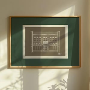 Puede incluir: Un dibujo arquitectónico enmarcado de un edificio, con una fachada detallada con ventanas arqueadas y una entrada central. La obra de arte está en un marco de madera con un passe-partout verde, colgada en una pared blanca. El dibujo está en una paleta de colores neutros.