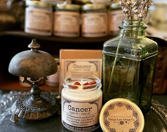 Pode incluir: Uma vela branca com um rótulo castanho que diz "Câncer 21 de junho - 22 de julho Protetor e nutritivo. Pode ser leal até a culpa. Intuição e imaginação muito fortes! Vintage Luxe Design Co."