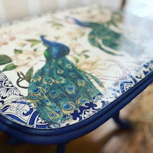 May include: A blue and white painted table with a peacock design on the top. The table has a distressed finish and a rounded edge.