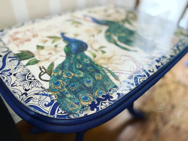 Pode incluir: Uma mesa pintada de azul e branco com um design de pav&atilde;o no topo. A mesa tem um acabamento desgastado e uma borda arredondada.