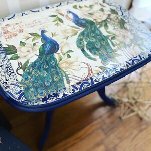 Pode incluir: Uma mesa auxiliar azul com tampo branco com um design de pav&atilde;o e o texto "J. Darbar". A mesa tem uma borda com um padr&atilde;o azul e branco.