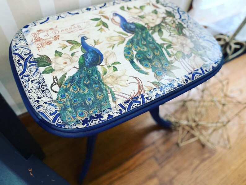 Pode incluir: Uma mesa auxiliar azul com tampo branco com um design de pav&atilde;o e o texto "J. Darbar". A mesa tem uma borda com um padr&atilde;o azul e branco.
