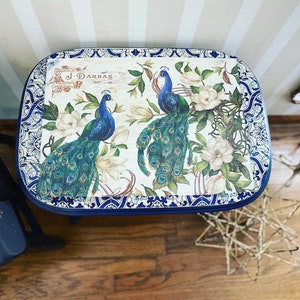 Pode incluir: Uma mesa de madeira com tampo azul e branco com um design decorativo com pav&otilde;es e flores. O design inclui o texto "J. Darbas".