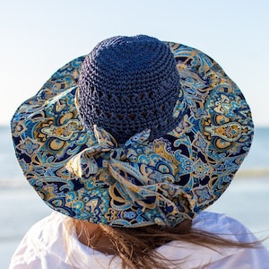 K&ouml;nnte beinhalten: Eine Frau tr&auml;gt ein wei&szlig;es Hemd und einen blauen und gelben gemusterten Sonnenhut mit einer blauen H&auml;kelkrone.